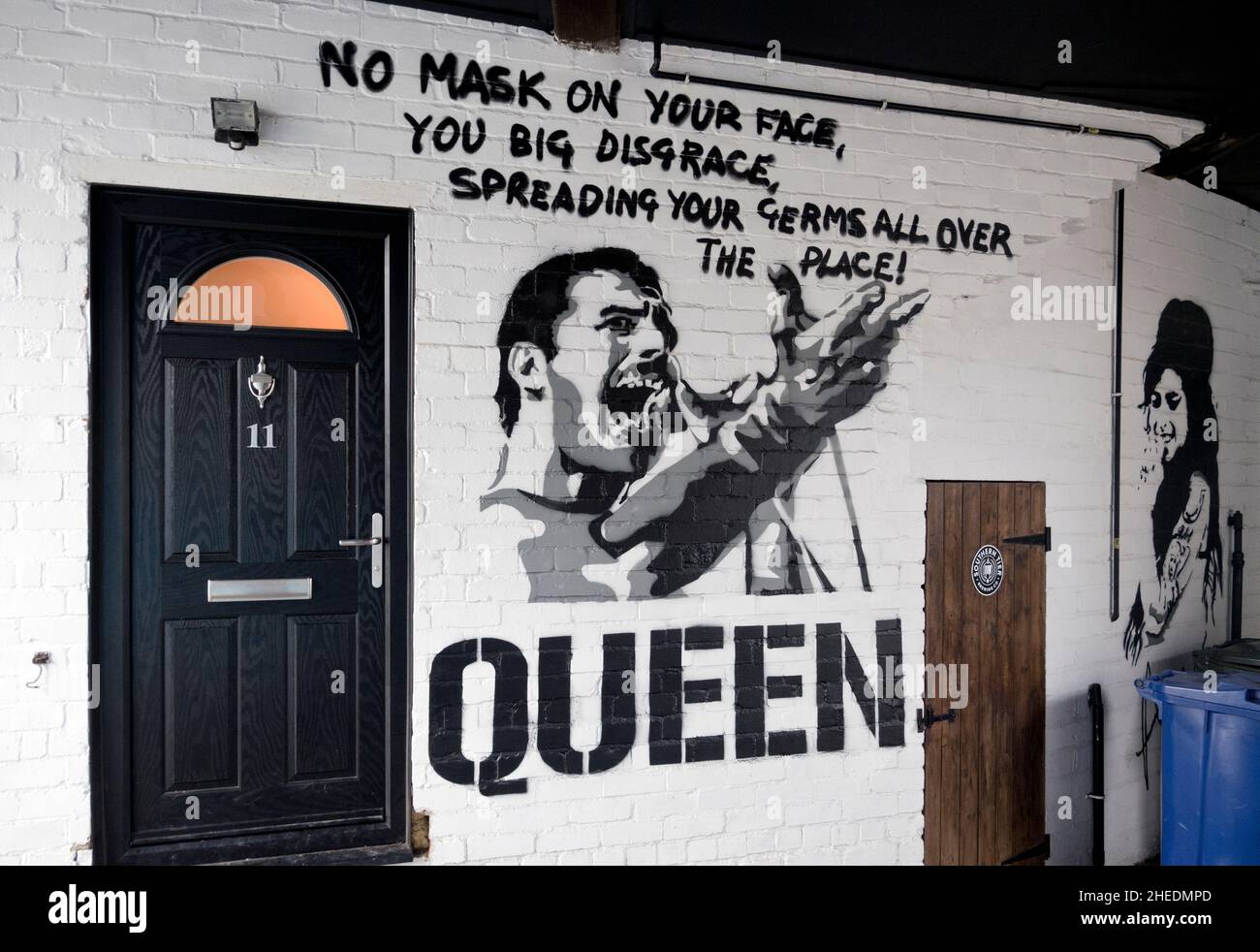 Maschera Covid-19 indossando Freddie Mercury / Queen graffiti art, Skipton, North Yorkshire, UK. Amy Winehouse graffiti a destra. Foto Stock