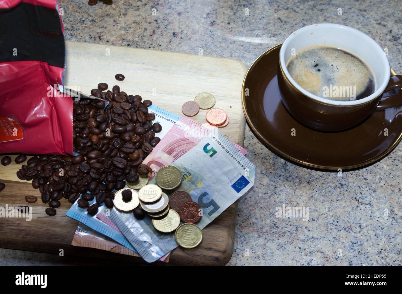 Immagine simbolica dell'aumento dei prezzi del caffè: Sacchetto di caffè aperto, chicchi di caffè, denaro e tazza di caffè piena Foto Stock