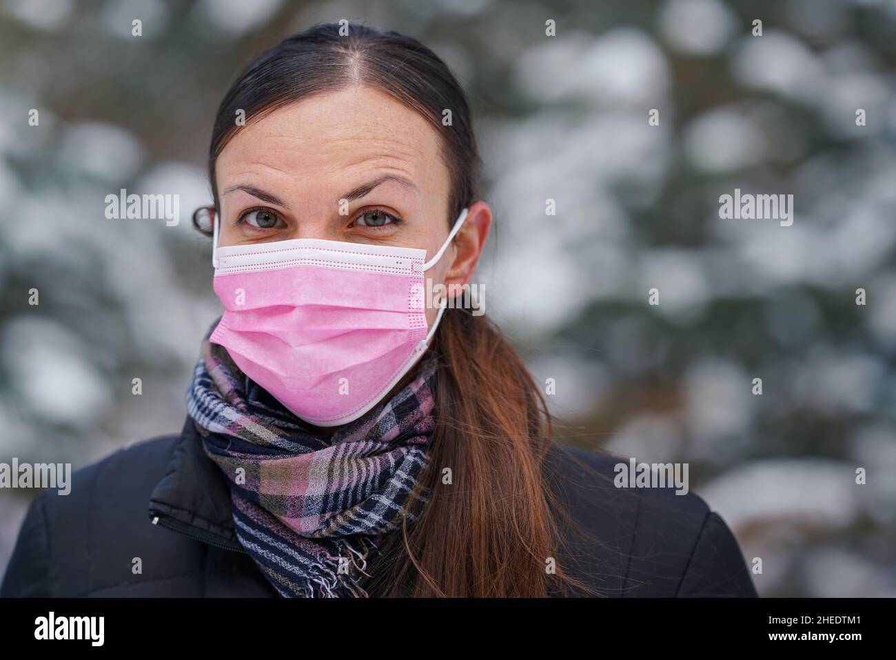 Giovane donna in giacca invernale con maschera monouso rosa virus del viso monouso Foto Stock
