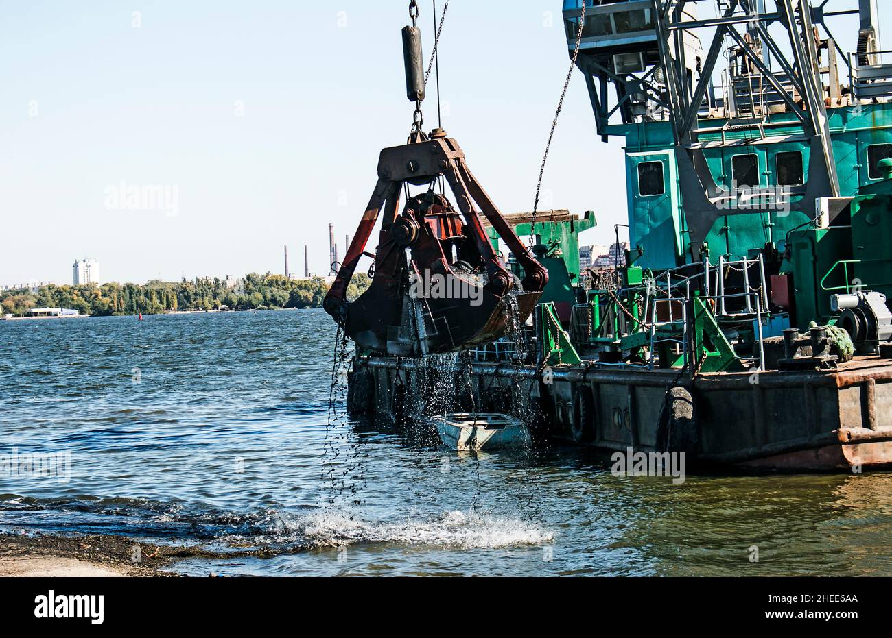 Pulire l'isola appena formata dai rifiuti industriali sul Dnieper con una draga. La benna scarica il fango sulla chiatta. Concetto di ecologia. Foto Stock