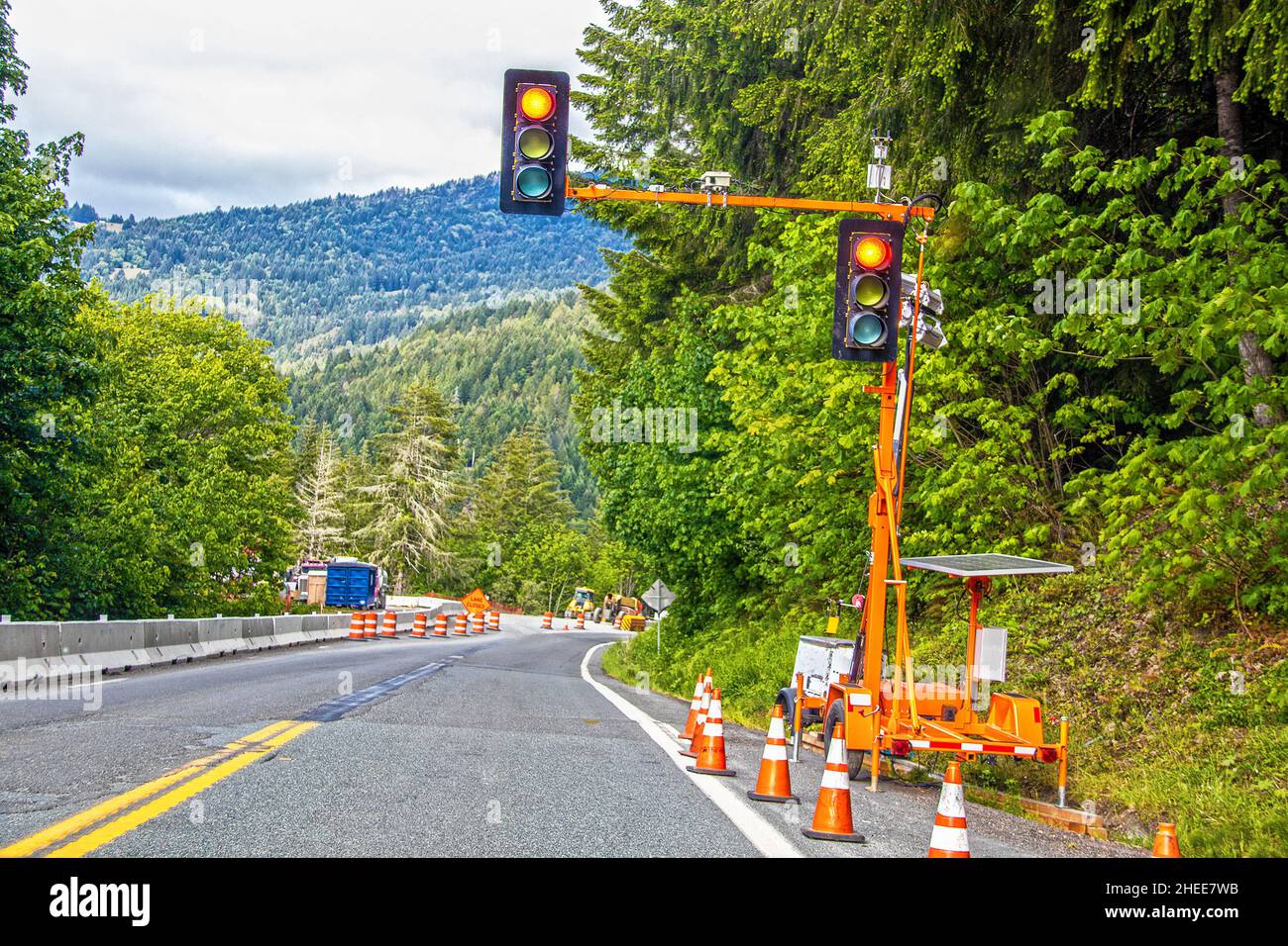 Semaforo portatile a energia solare in cantiere in montagne coperte di alberi con attrezzature e coni stradali Foto Stock