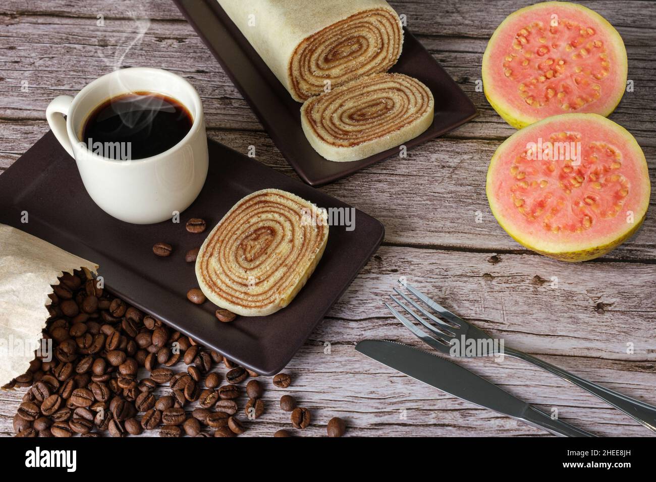 Fetta di Bolo de rolo circondata da guava, posate, tazza e chicchi di caffè. Foto Stock