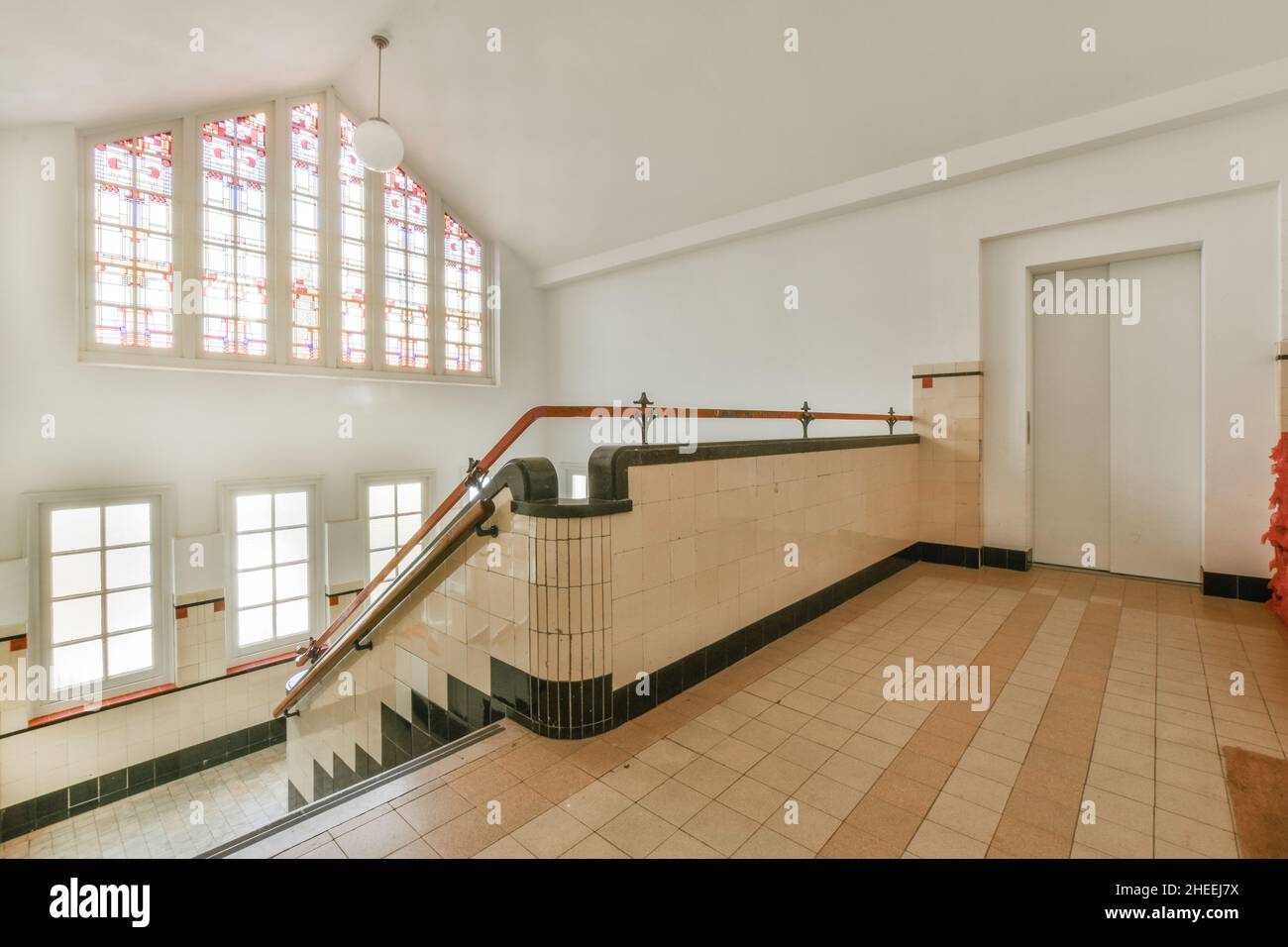 All'interno di un ampio salone con pareti piastrellate e pavimento e scala con corrimano e finestre in vetro con elementi a mosaico Foto Stock