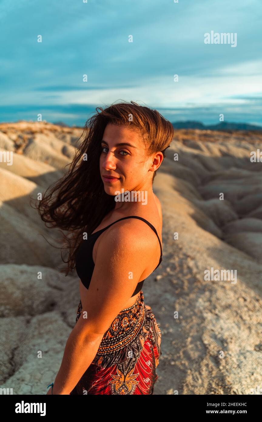 Attraente brunetta da donna con capelli lunghi ondulati e con la parte superiore nera che guarda la macchina fotografica alla luce del sole Foto Stock
