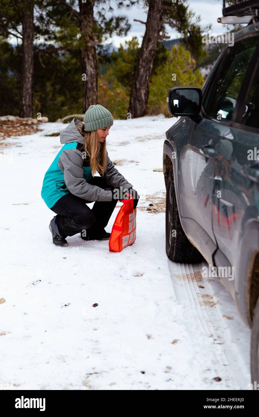Donna che prende catene di gomma da neve per auto da borsa di kit di riparazione vicino bloccato auto nella neve Foto Stock