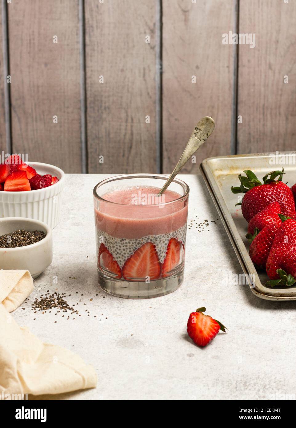 Gustoso budino con semi di chia e fette di fragole fresche poste sul tavolo vicino agli ingredienti per una colazione sana Foto Stock