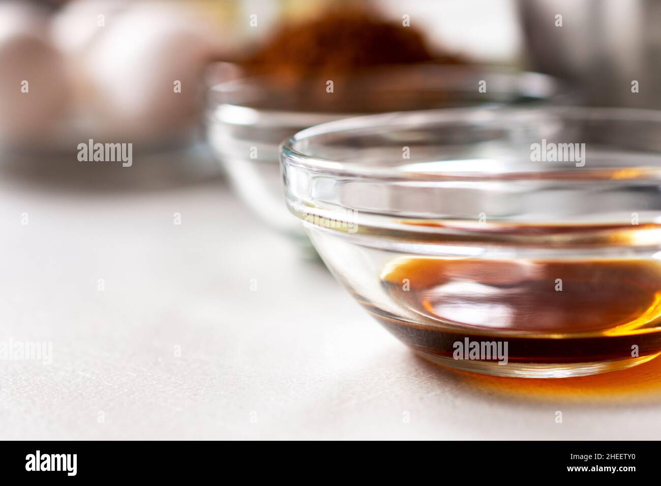Una vista closeup della vaniglia in una ciotola di vetro. Altri ingredienti di cottura sfocati sullo sfondo. Profondità di campo poco profonda. Spazio di copia in basso a sinistra. Foto Stock