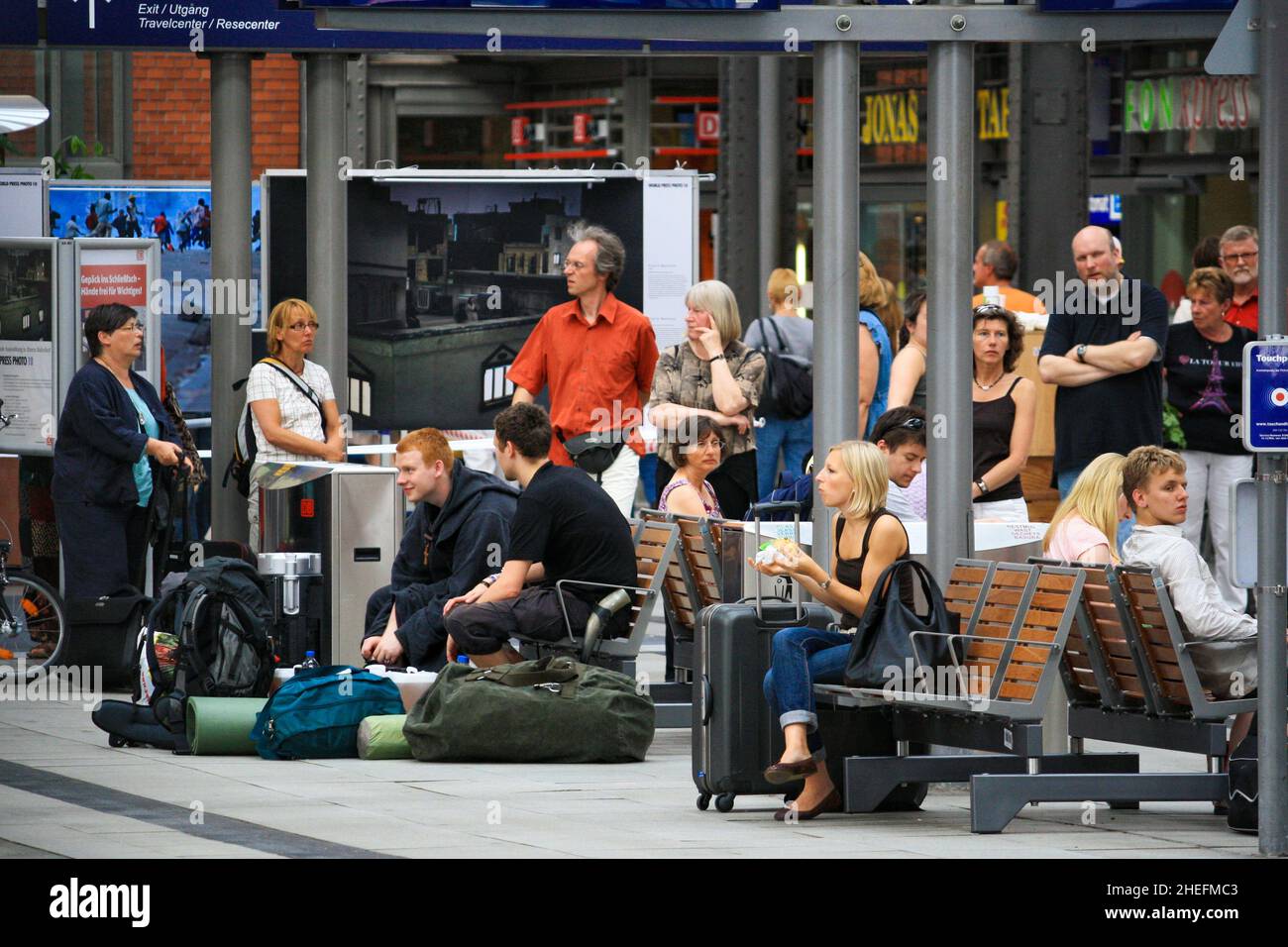Folla di cittadini europei seduti e in piedi in attesa della partenza sul binario della Hauptbahnhof di Amburgo o della stazione ferroviaria centrale in estate. Foto Stock
