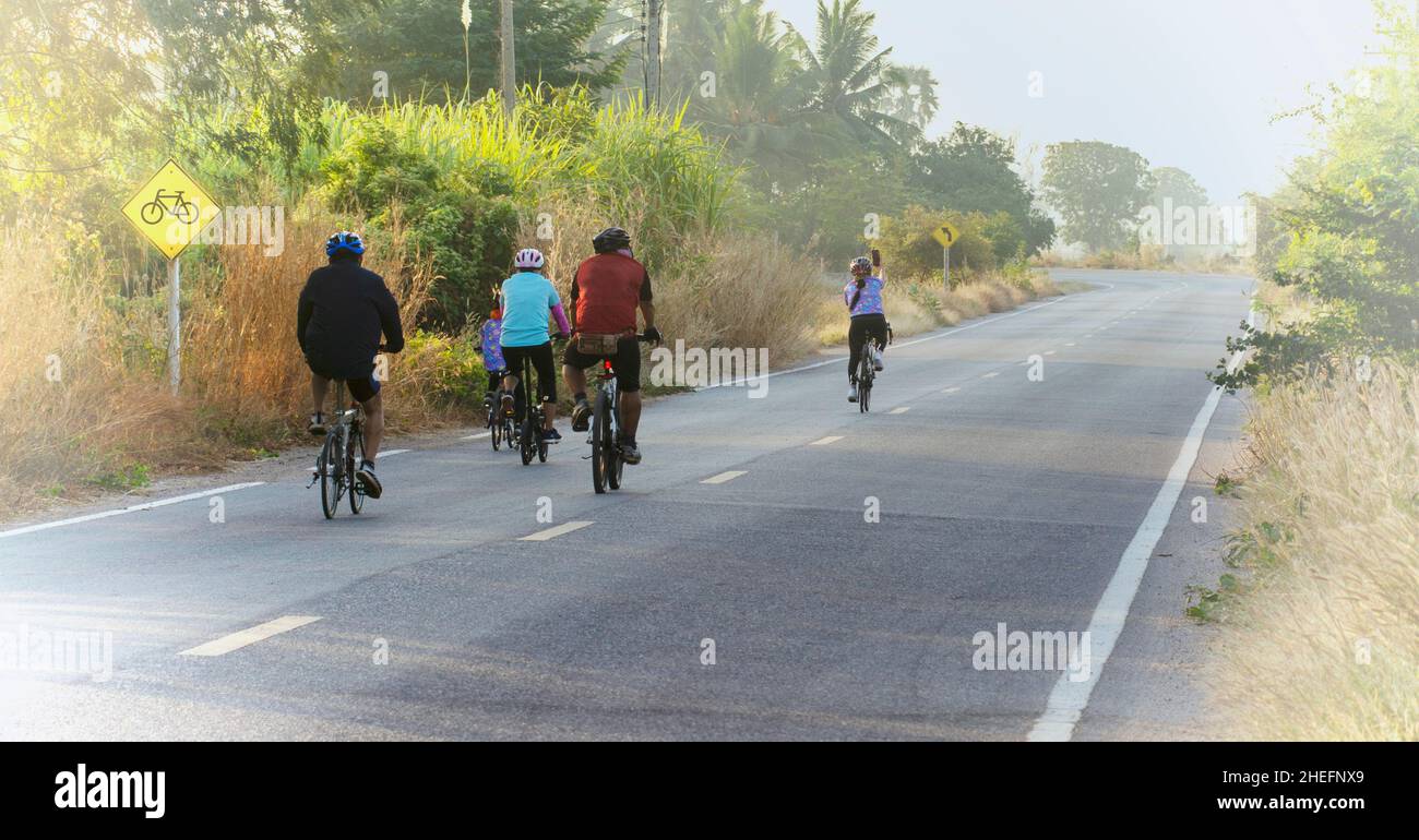 Vista posteriore di famiglia giri in bicicletta per una buona sana su strada rurale presto al mattino. Foto Stock
