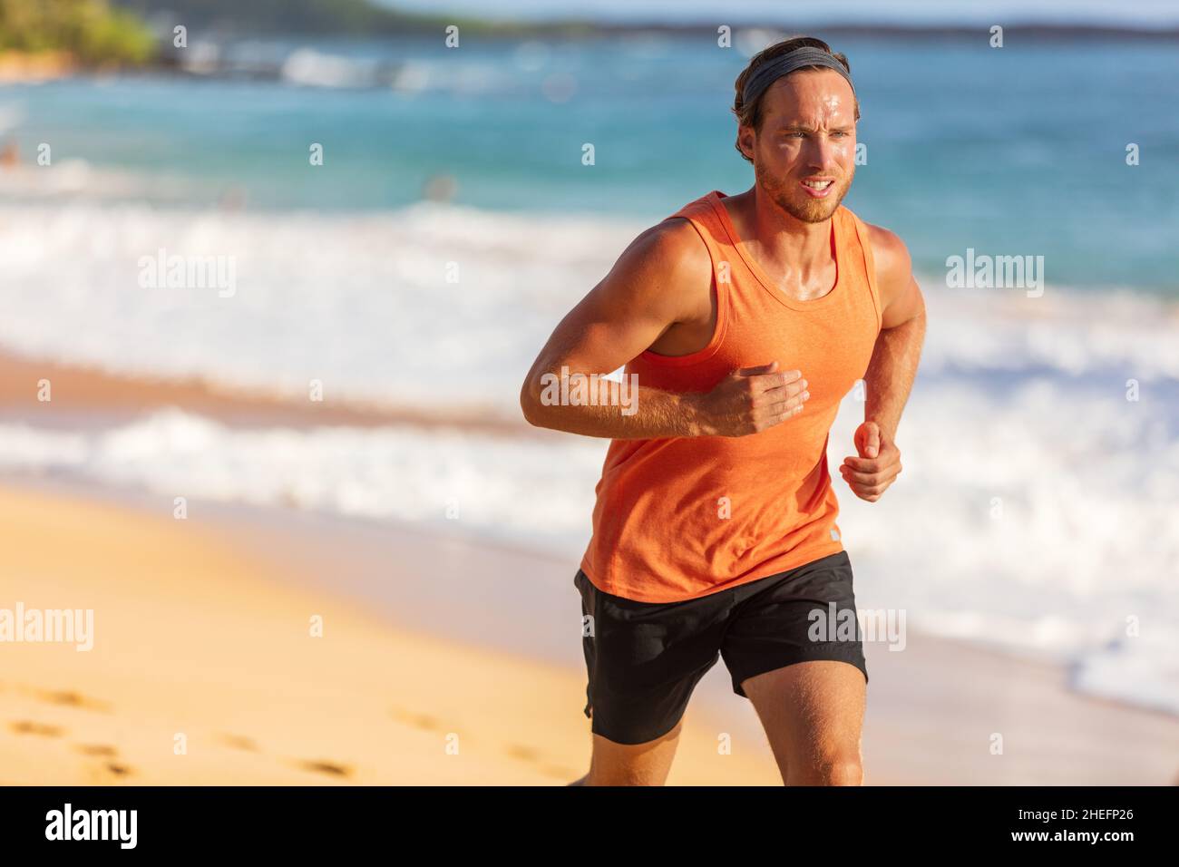 Atleta che corre in spiaggia sudando allenamento cardio su intenso hiit allenamento a temperatura estiva. Stile di vita sportivo maschile Foto Stock