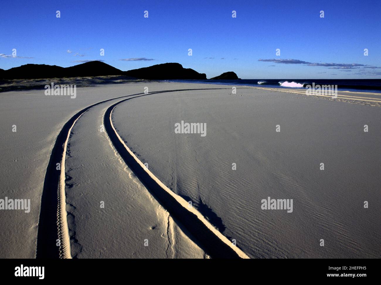 Foto a colori dei tracciati dei veicoli su una spiaggia con onde che si infrangono sulla riva, Sand Bar Beach, New South Wales, Australia, 2005. Foto Stock