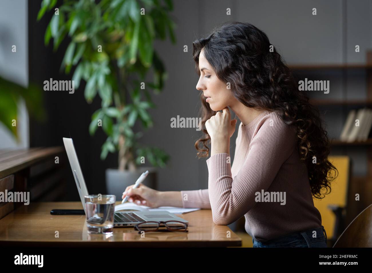 Giovane accademico femminile che guarda lo schermo del laptop, facendo ricerche online mentre lavora in biblioteca Foto Stock