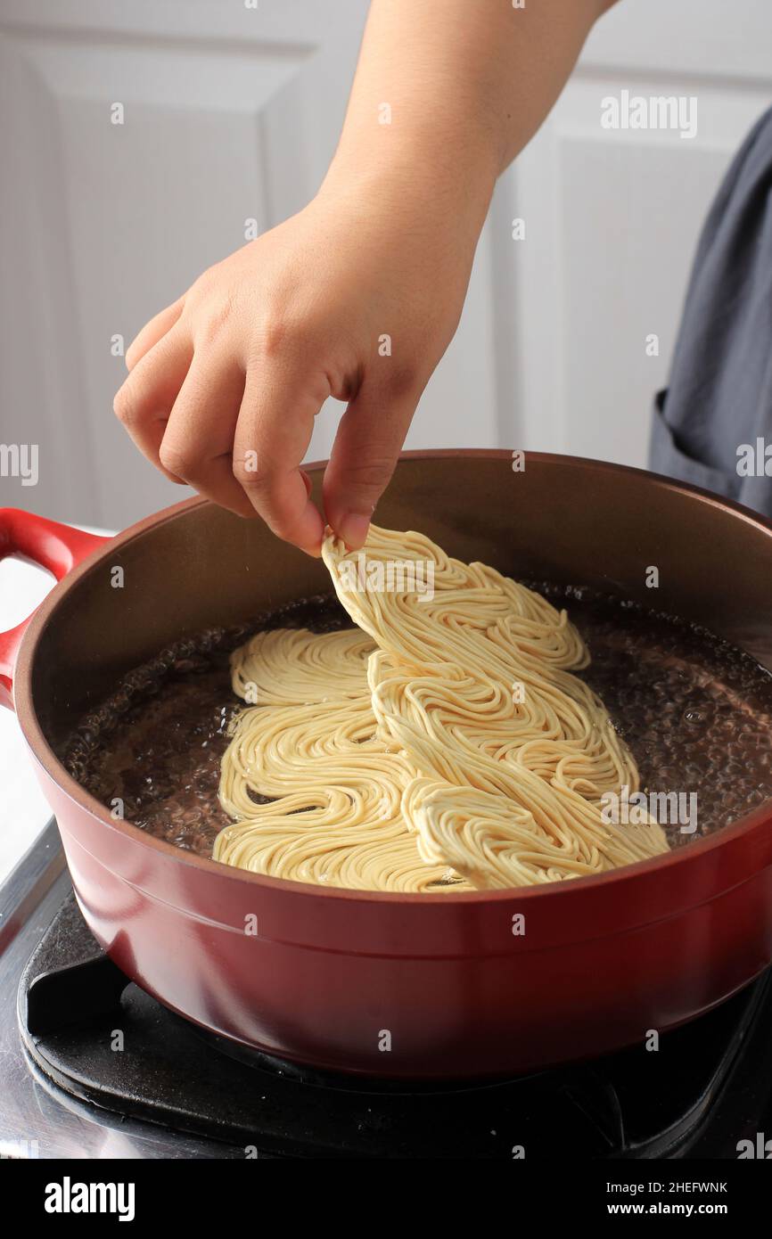 Chef Asiatico femmina bollente Asiatico Noodle secco (mie Telur) su una padella rossa, aggiungere Noodle alla padella, attività di cucina casalinga. Cottura fase per fase Foto Stock