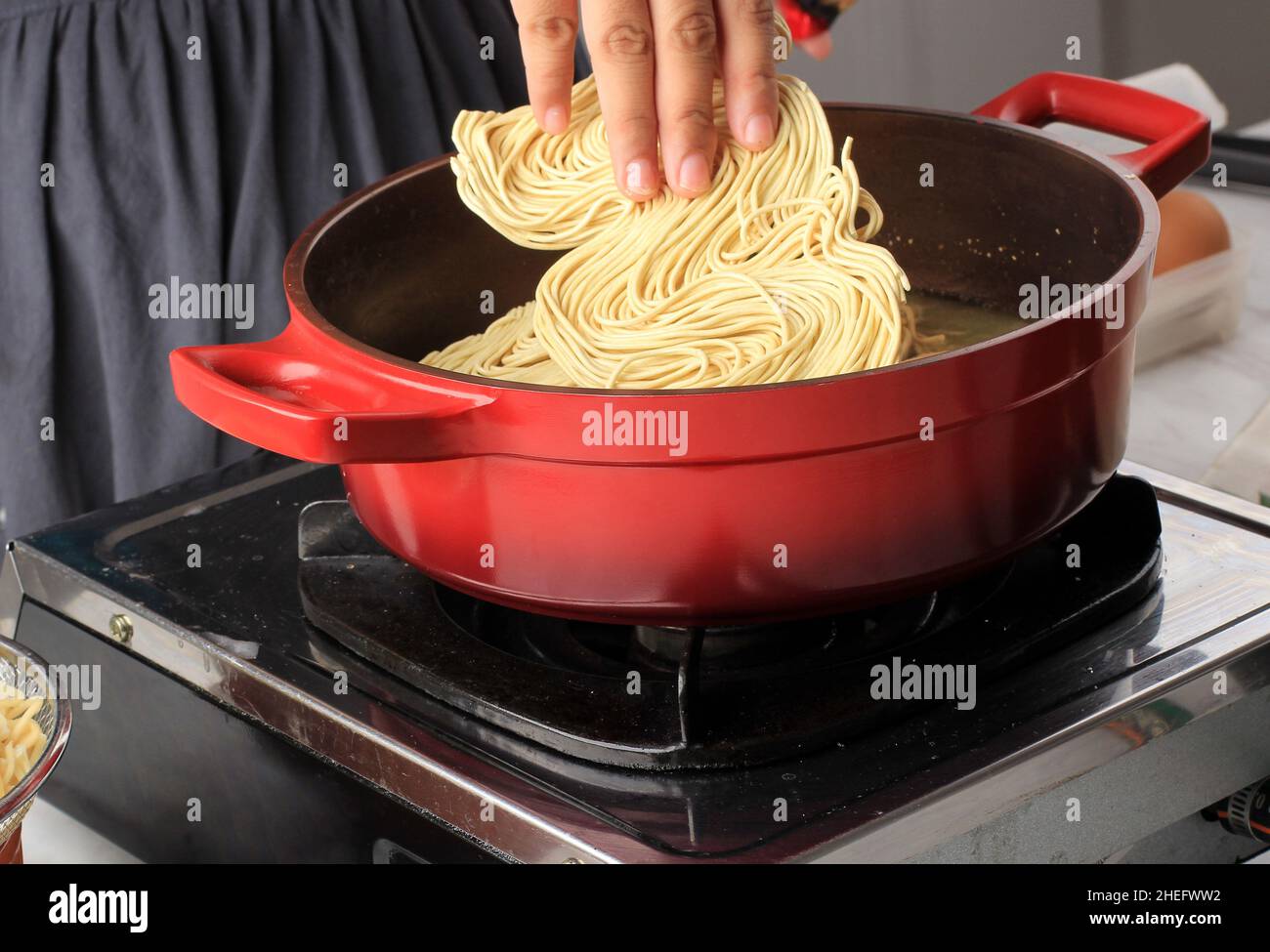 Mettere a mano la noodle in acqua bollente sulla padella. Preparare la noodle istantanea (mie telur). Processo di cottura in cucina Foto Stock