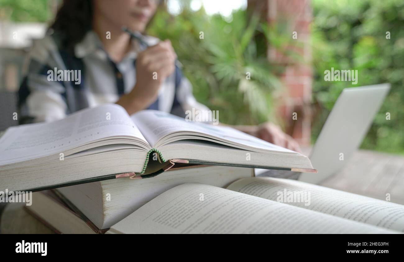 Libri sul tavolo con donna e computer portatile in background. Impostazione Home. Foto Stock