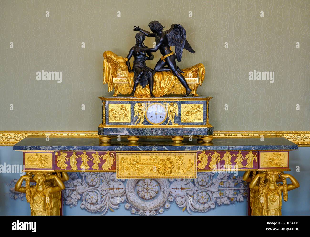 Un antico orologio decorato con bassorilievi dorati di antica vita e con una scultura mitologica in cima Foto Stock