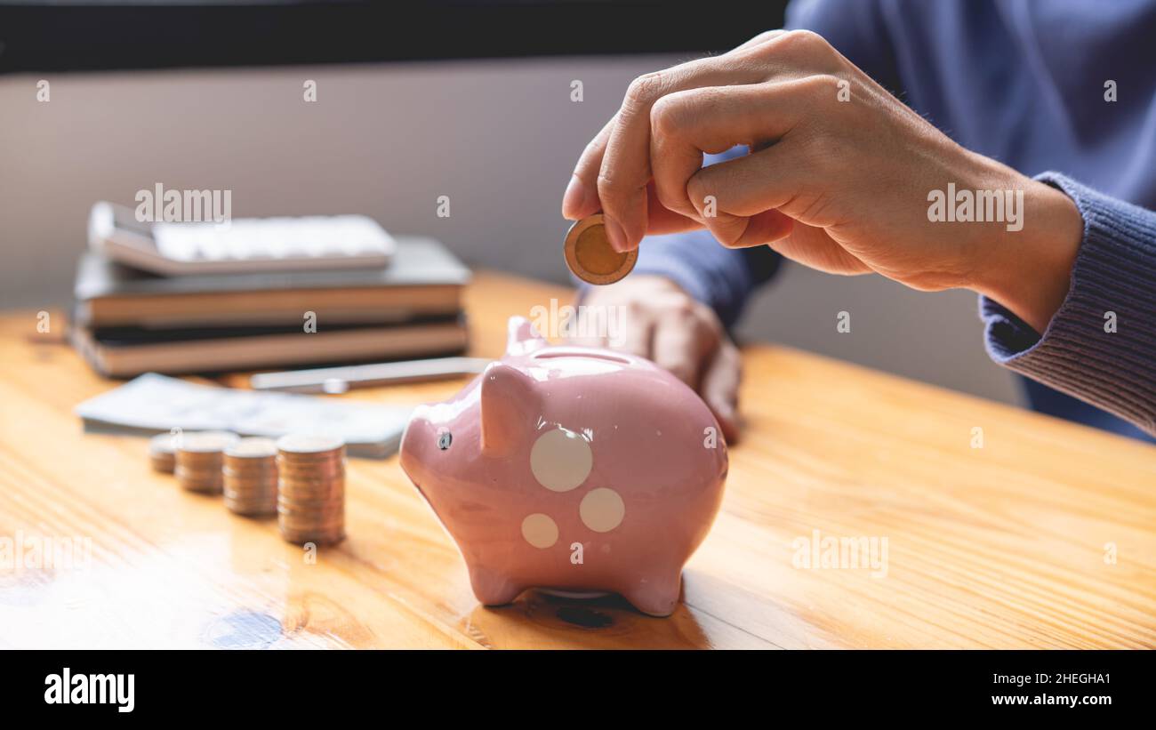 concetto di risparmio il maschio che raccoglie la sua moneta per cadere in una banca rosa del piggy come i suoi soldi che risparmiano in su per questo mese. Foto Stock