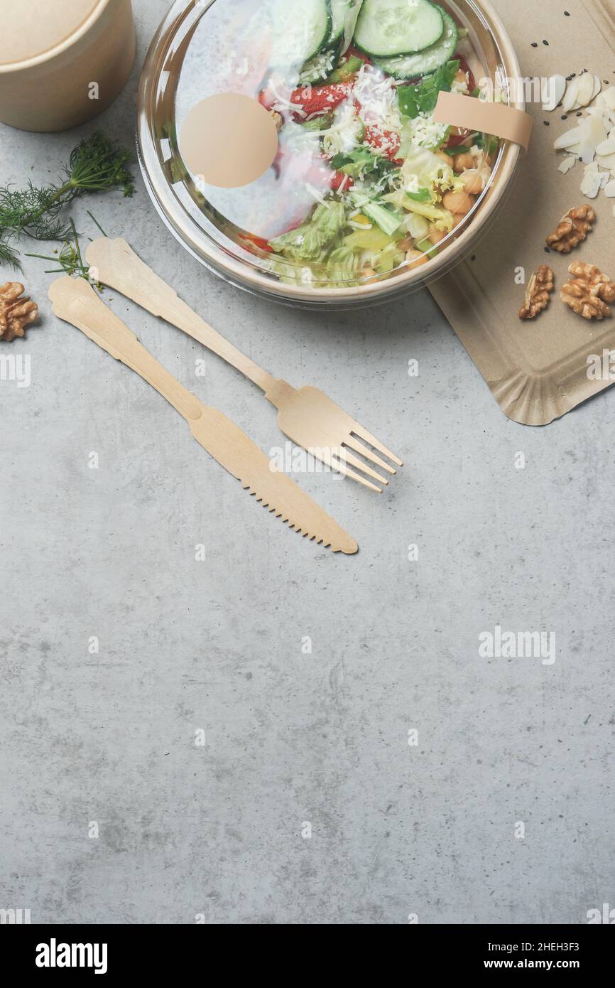Sano pranzo con insalata da portare via in un imballaggio ecologico con posate in legno. Fornitura sostenibile di cibo su sfondo grigio. Vista dall'alto. Telaio Foto Stock