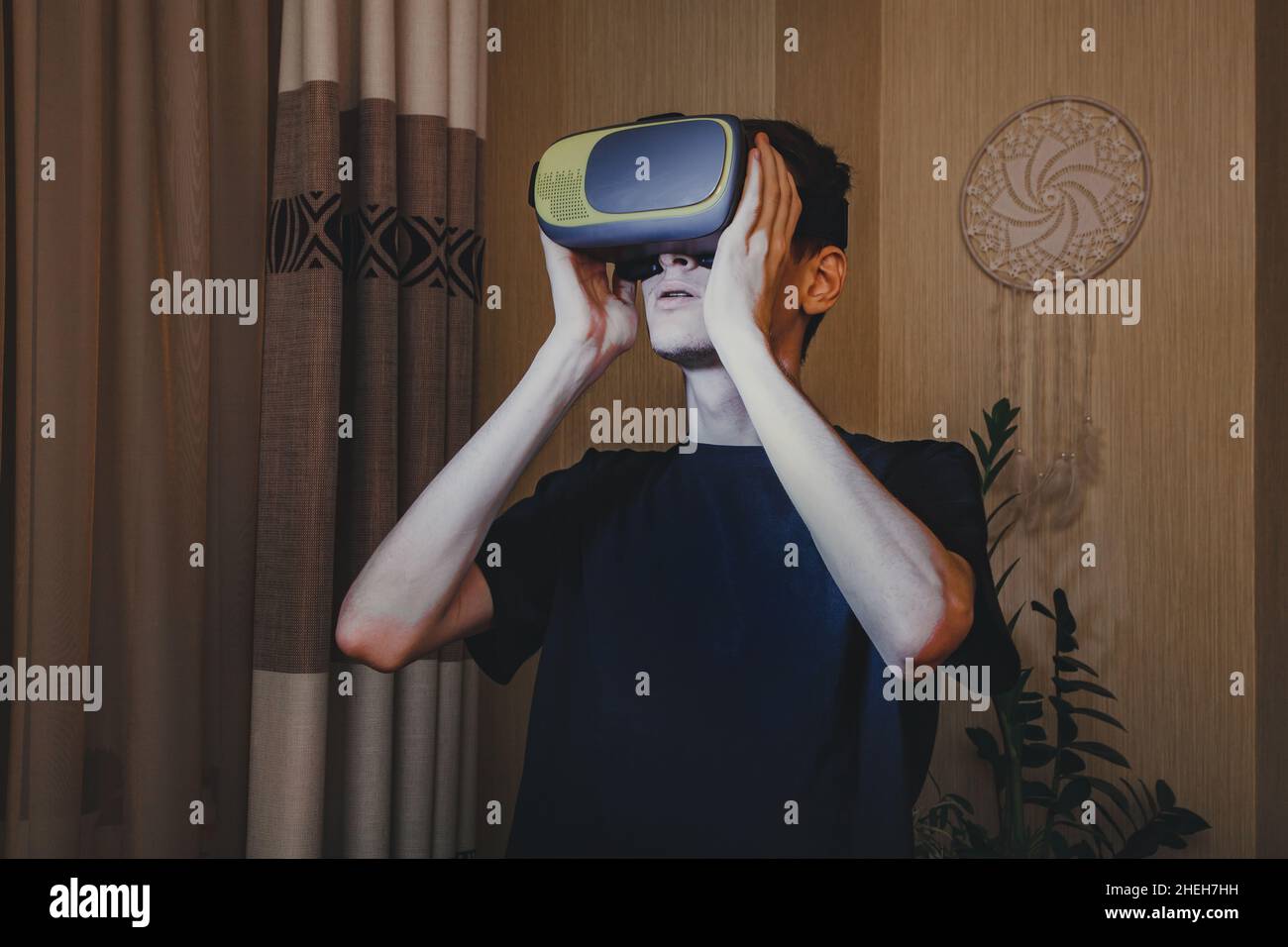 Giovane uomo in un casco VR che guarda in realtà virtuale all'interno della casa. Foto Stock