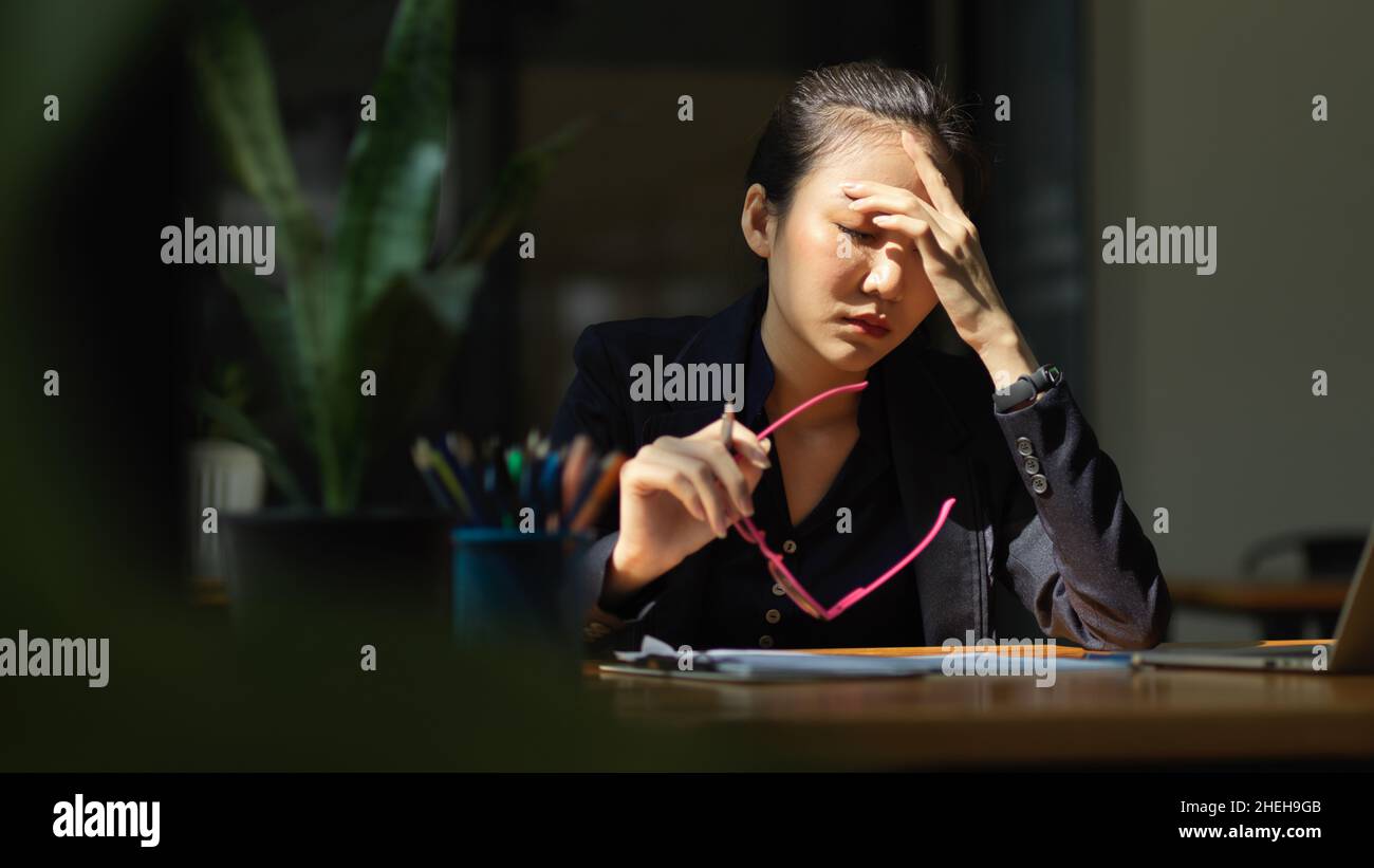 Una donna d'affari ha un mal di testa o affaticamento degli occhi dopo aver lavorato troppo. Stressato, affaticamento degli occhi, esaurito. Foto Stock