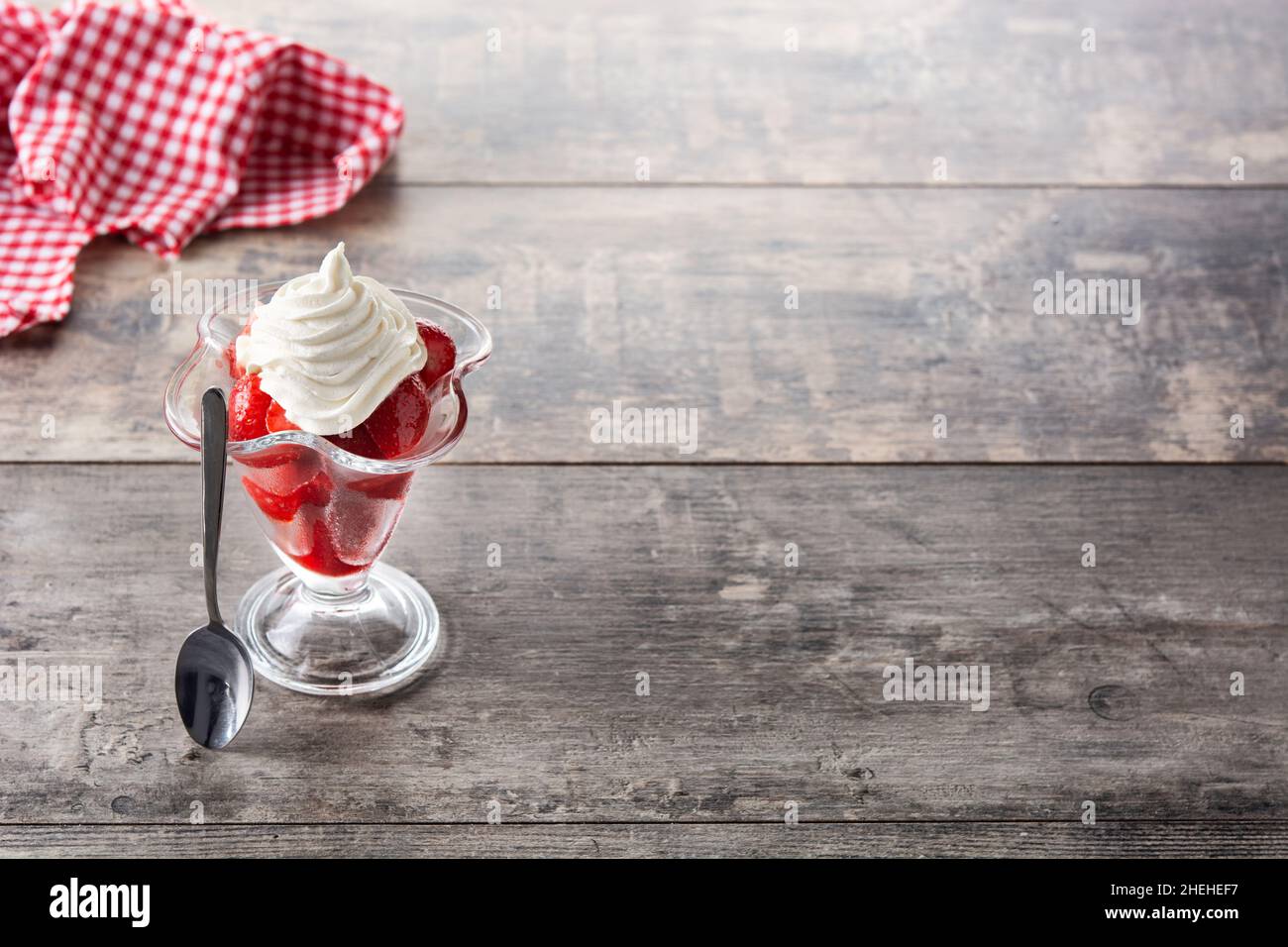 Fragole e panna montata in un bicchiere di gelato su un tavolo di legno Foto Stock