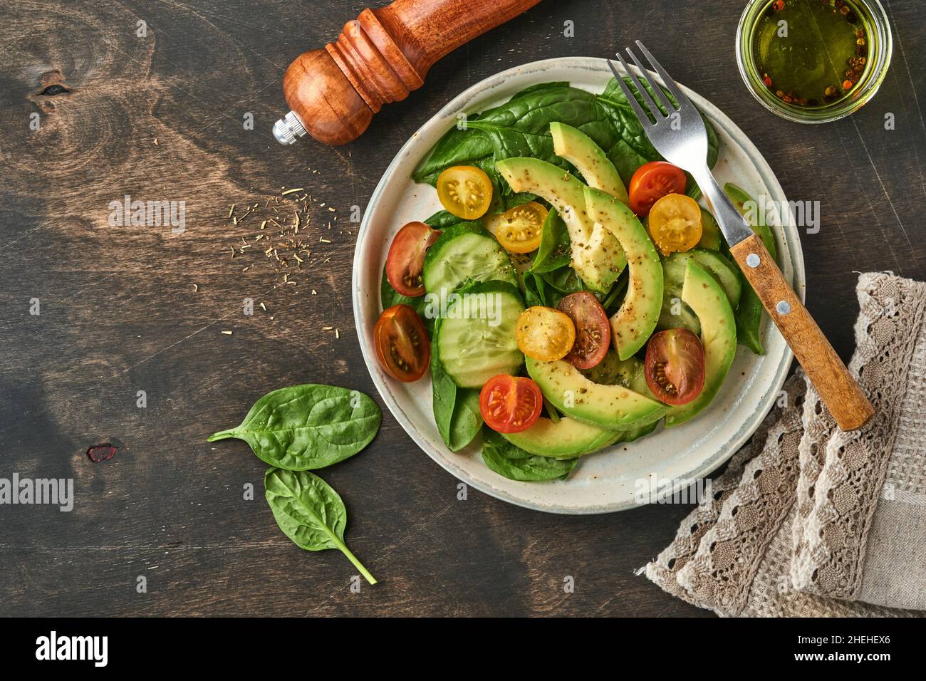 Avocado, rosso, giallo, pomodoro di amarena, spinaci e cetriolo insalata fresca con spezie pepe e olio d'oliva in ciotola grigia sfondo vecchio tavolo di legno. Foto Stock