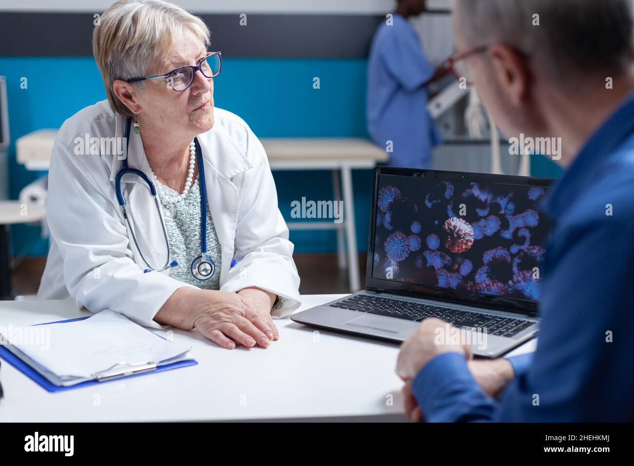 Primo piano di un medico e di un paziente che discute di informazioni sui batteri virus sul computer portatile. Medico generico che utilizza il computer per spiegare la rappresentazione visiva di covid 19 batteri per l'uomo anziano. Foto Stock