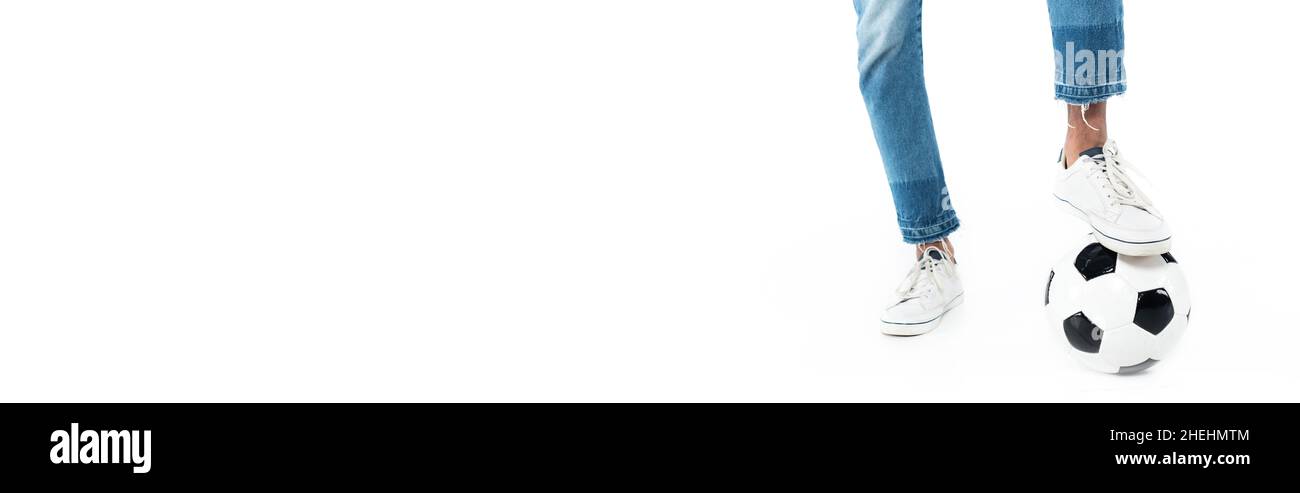 vista ritagliata dell'uomo afro-americano in jeans e sneakers che giocano a calcio su bianco, banner Foto Stock