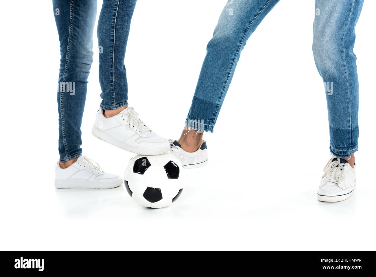 vista ritagliata di amici multietnici in jeans e sneakers che giocano a calcio su bianco Foto Stock
