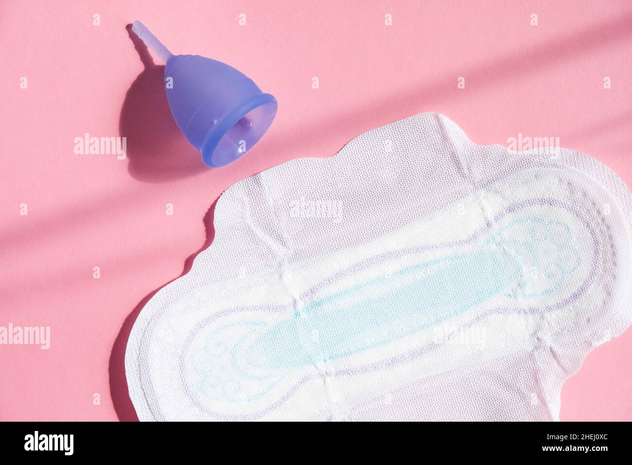 Tazza mestruale viola contemporanea e imbottitura sanitaria donna giacciono su sfondo di colore rosa chiaro da vicino vista dall'alto Foto Stock