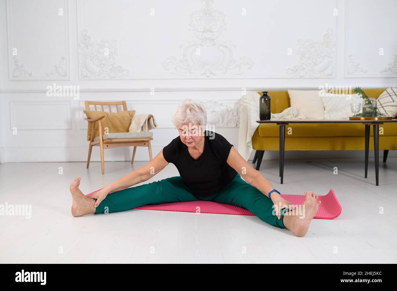 Donna sportiva anziana che fa yoga mentre guarda il tutorial sul laptop Foto Stock