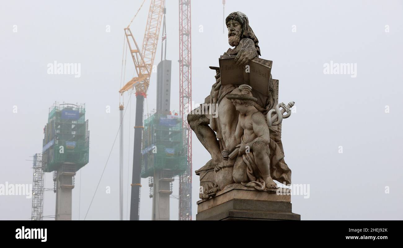 Magdeburg, Germania. 11th Jan 2022. Una figura allegorica dello scultore tedesco Emil Hundrieser, destinata a simboleggiare il commercio, è vista sul ponte a pedaggio prima che una testa di traliccio per il nuovo ponte di tralicci sia sollevata in posizione. I componenti in acciaio, che pesano circa 60 tonnellate, vengono collocati sui tralicci ad un'altezza di circa 60 metri con l'ausilio di una gru per impieghi pesanti. Il nuovo ponte sull'Alte Elba avrà quindi raggiunto l'altezza finale. Credit: Ronny Hartmann/dpa/ZB/dpa/Alamy Live News Foto Stock