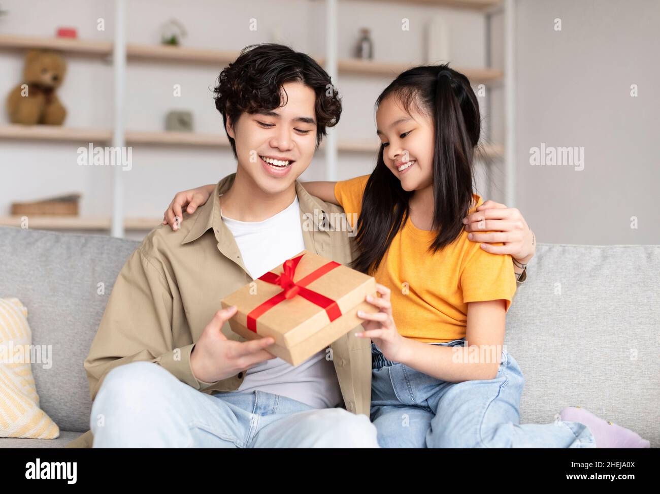 Sorridente giovane cinese felice riceve il regalo dalla figlia adolescente in camera interna Foto Stock