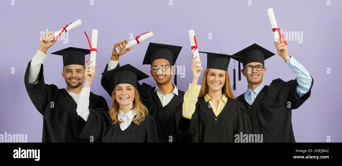 Felice studenti universitari diversi in berretti e camici che tengono in mano i diplomi e sorridenti Foto Stock