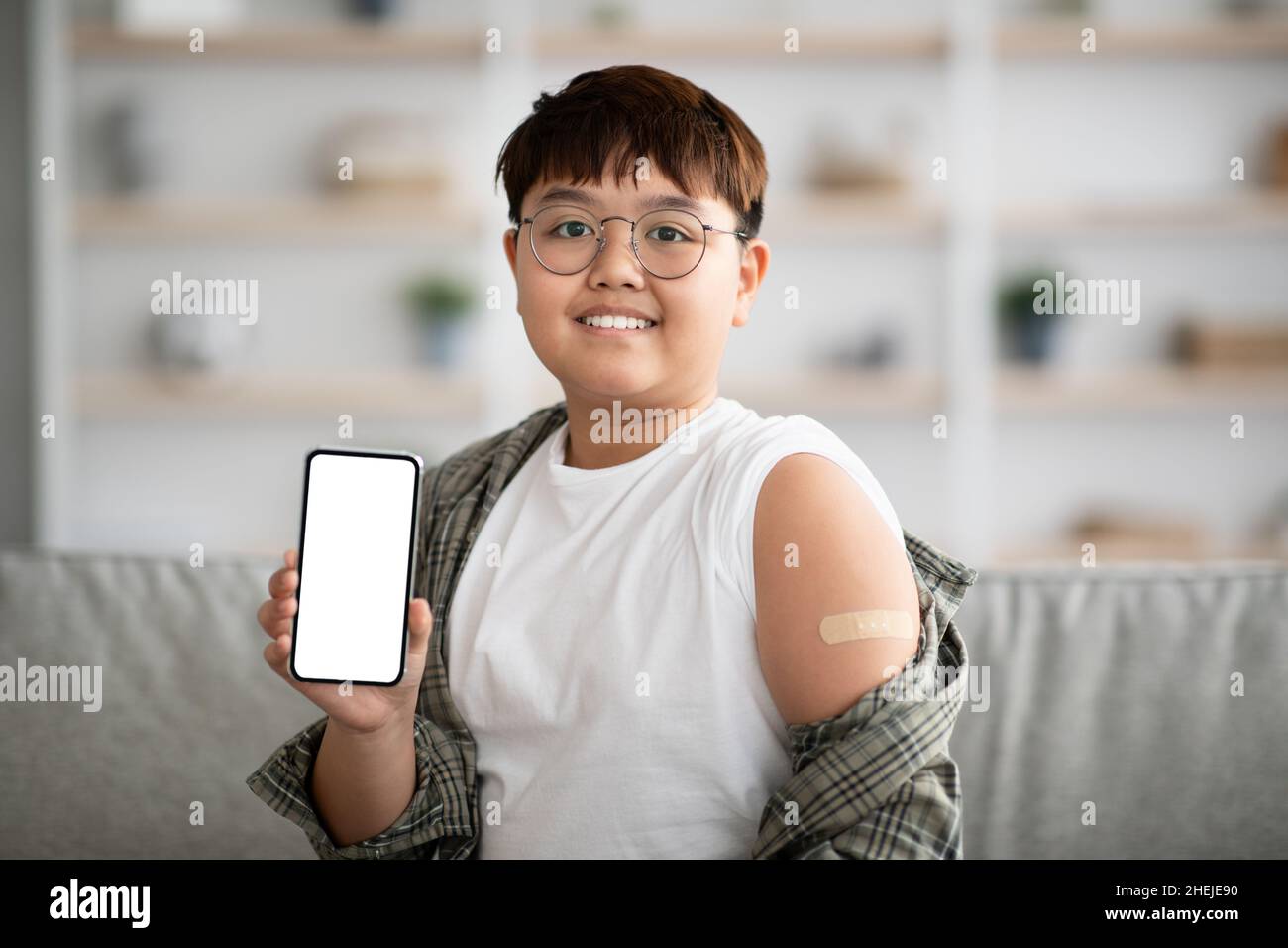 Adolescente asiatico vaccinato che mostra smartphone con schermo vuoto Foto Stock