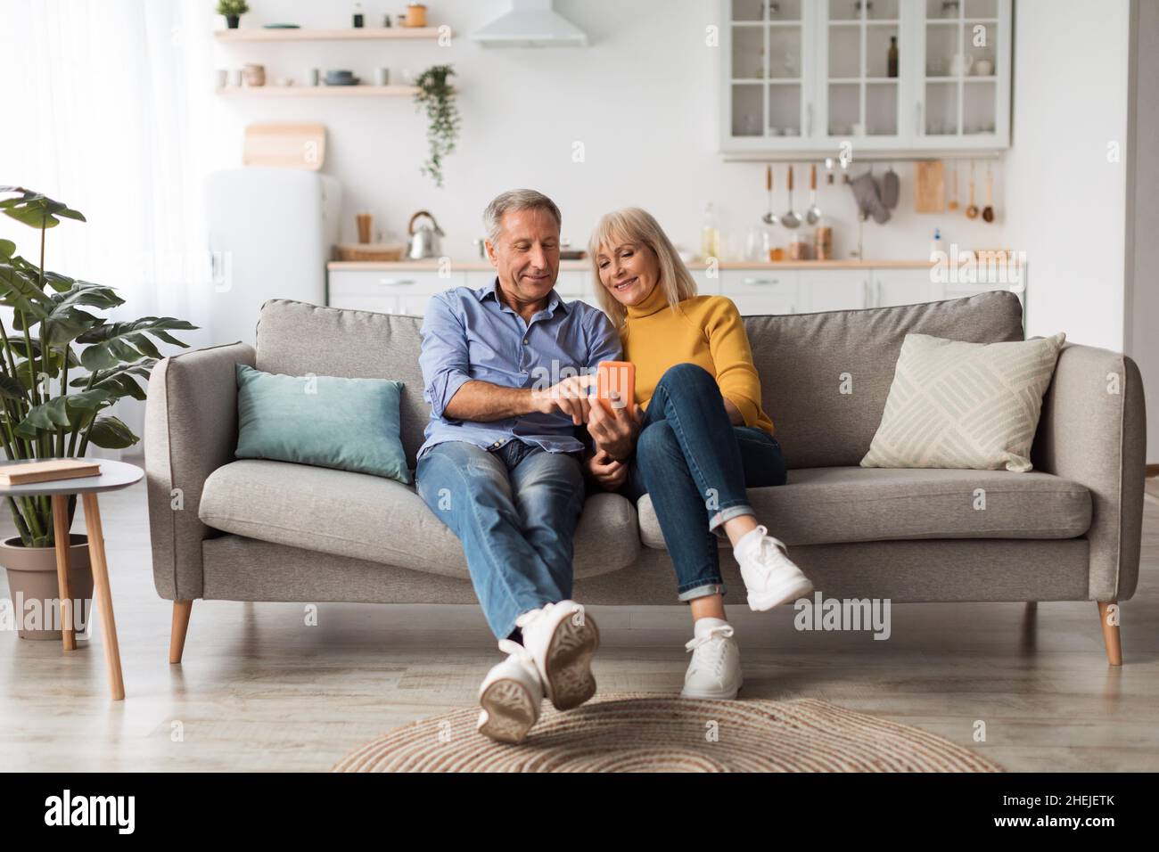 Felice marito e moglie maturi che usano lo smartphone seduto a casa Foto Stock