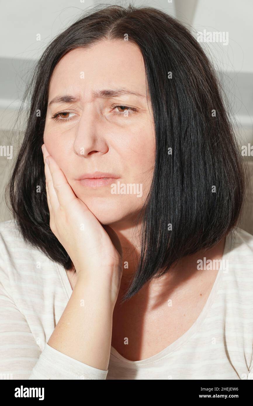 Donna matura in mezza età che tocca la bocca con una mano che soffre di mal di denti a casa. Concetto di salute dentale. Carie dentali, infiammazione o denti sensibili Foto Stock