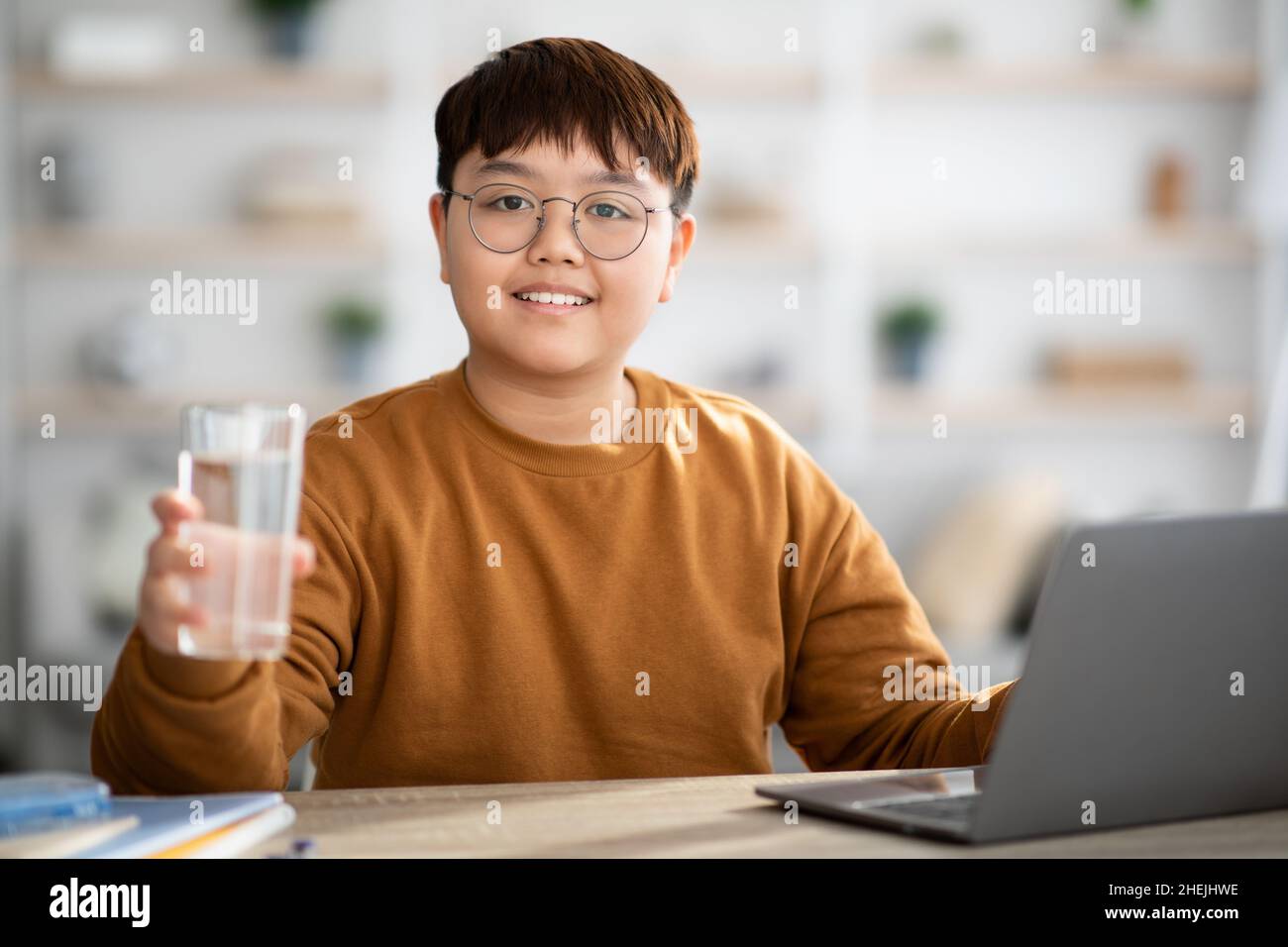 Adolescente asiatico sano che tiene un bicchiere d'acqua durante lo studio Foto Stock