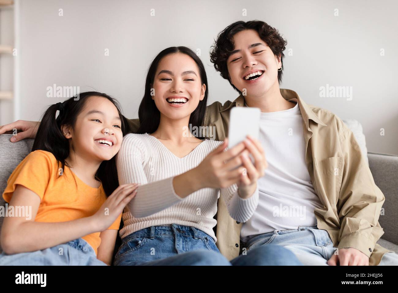 L'adolescenza ridente ragazza asiatica, mamma e papà giovani fanno selfie di famiglia su smartphone Foto Stock