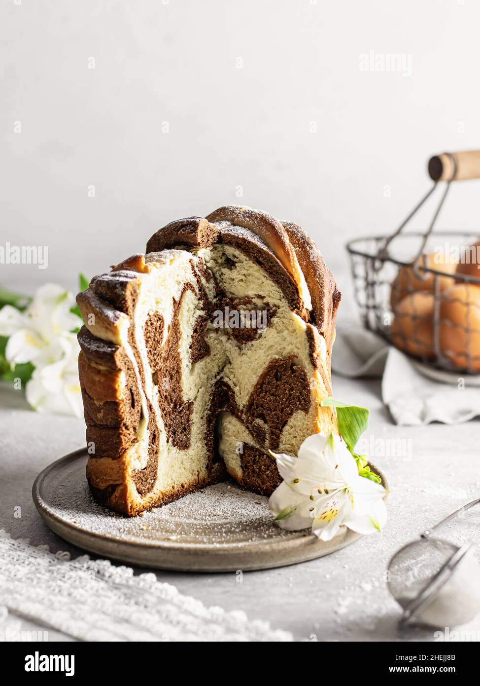 Composizione pasquale con torta marmorea tagliata, fiori e uova su sfondo chiaro Foto Stock