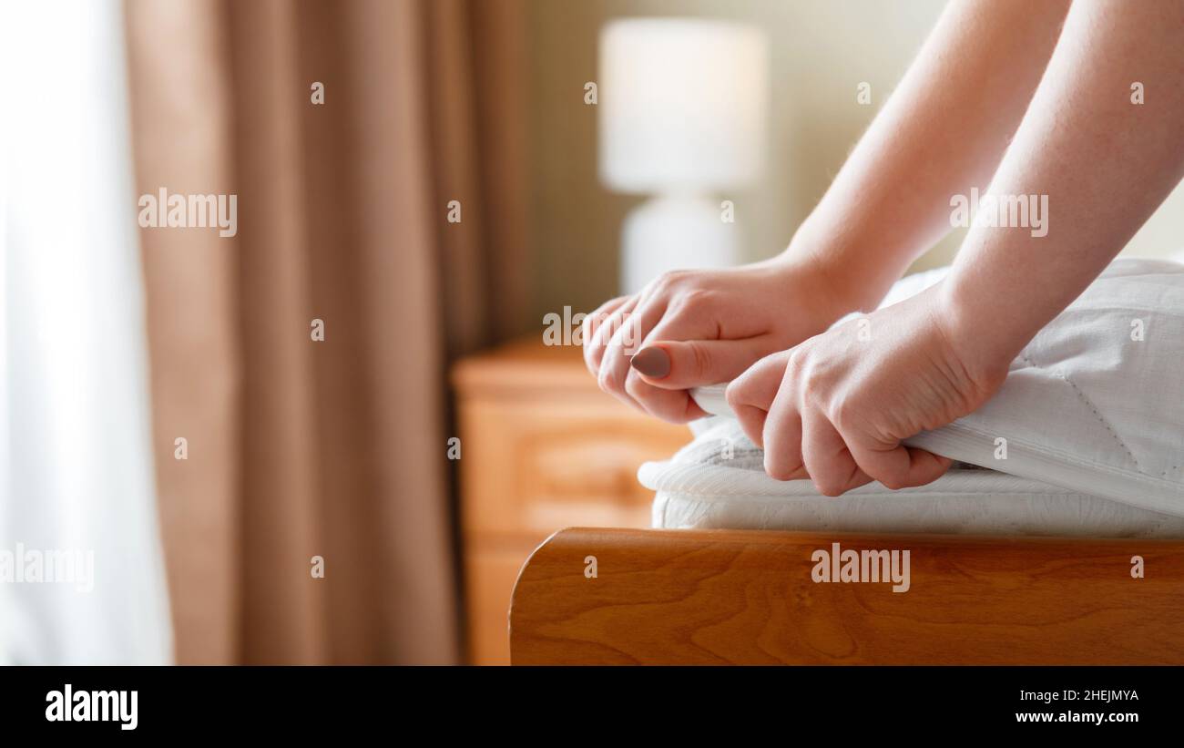 Le mani femminili si mettono sul nuovo materassino imbottito sull'angolo del materasso. Biancheria da letto a casa o in hotel. Il foglio è indossato su un materasso morbido e pulito. Protezione dallo sporco Foto Stock