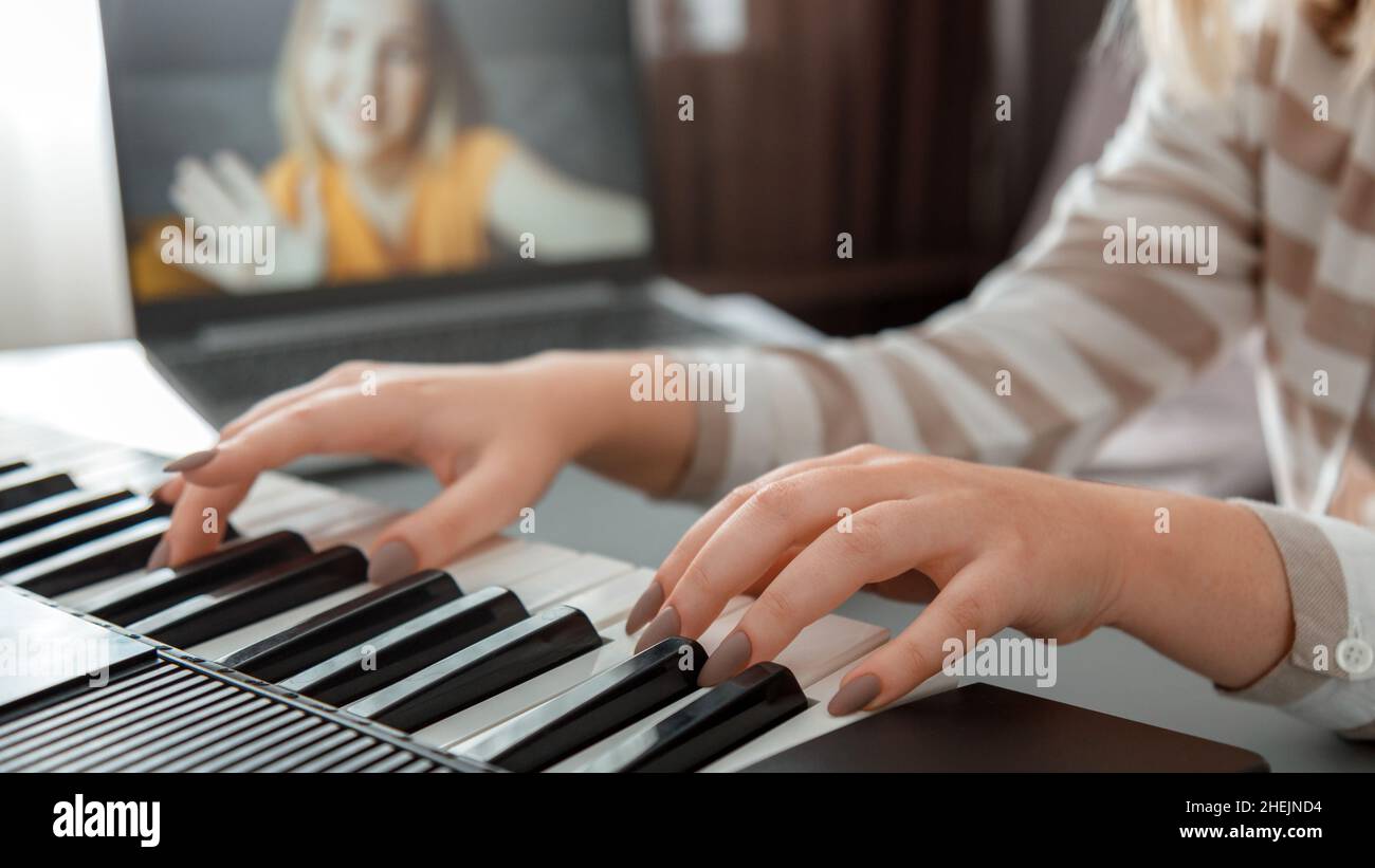 Donna che suona il pianoforte durante le videochiamate tramite computer portatile. Il pianista musicista delle mani femminili migliora le capacità di suonare il pianoforte in linea le classi con l'insegnante. Online Foto Stock