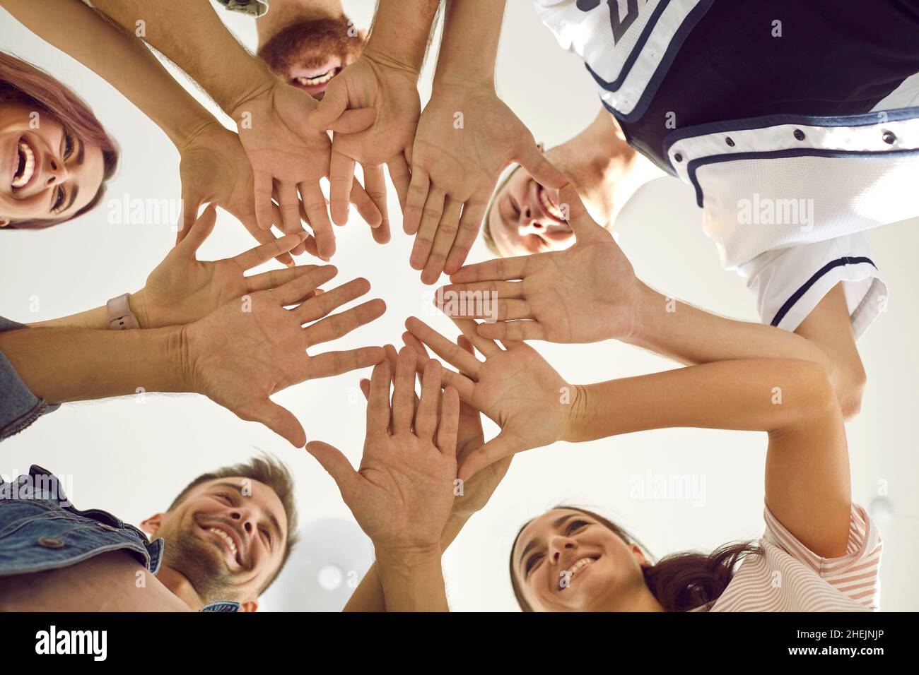 Vista dal basso di un gruppo di giovani felici e sorridenti che si mettono le mani insieme Foto Stock