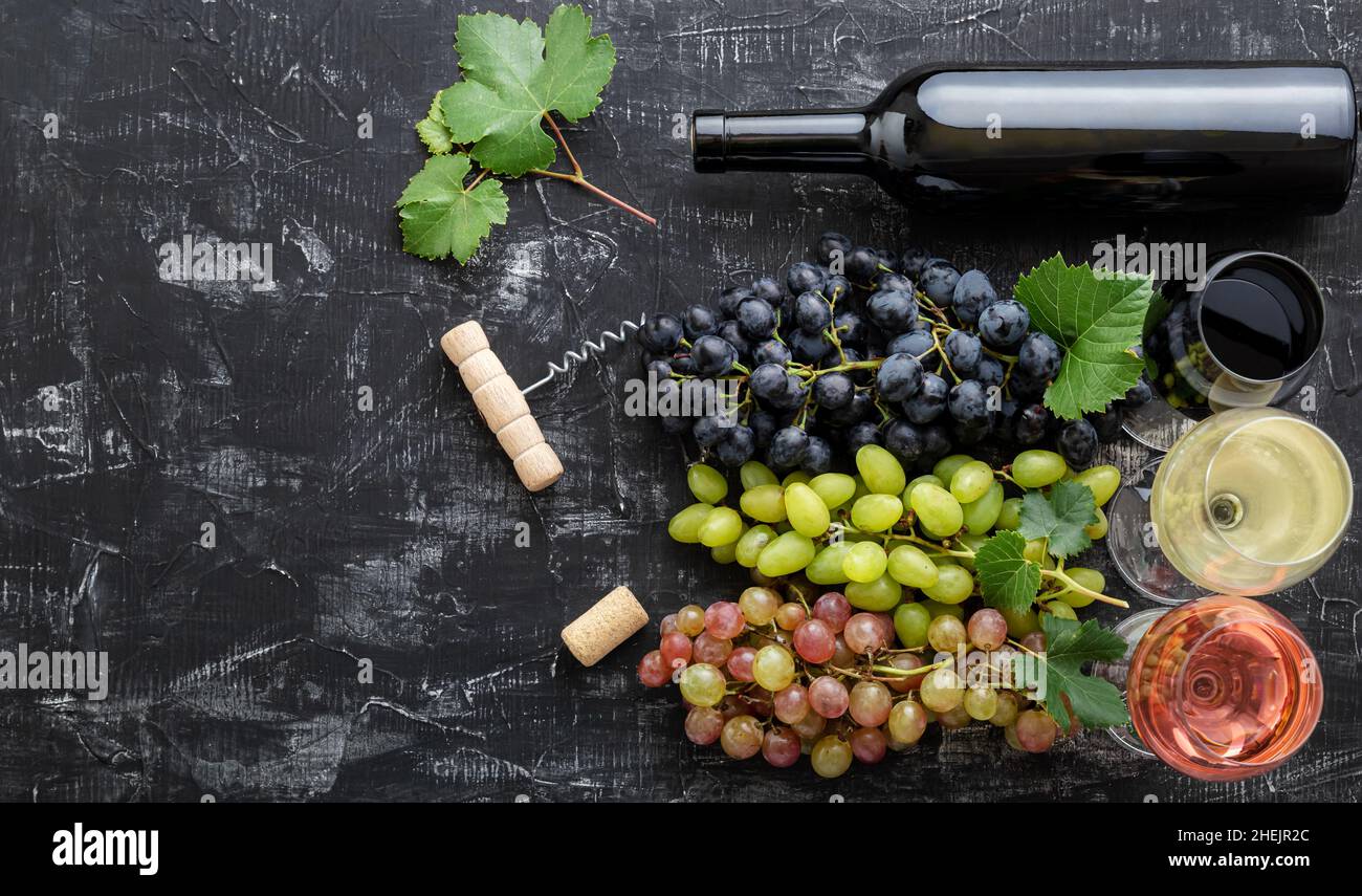 Assortimento di diversi tipi di vino e varietà di qualità. Degustazione di vino rosso rosato bianco in calici vicino alle uve bianche rosa e nere, bottiglia di vino rosso Foto Stock