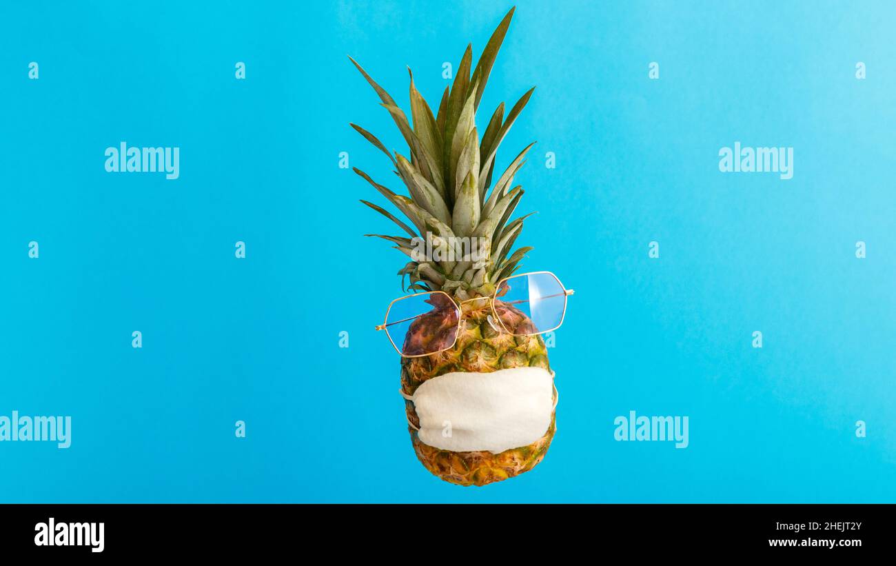 Ananas faccia divertente in occhiali da sole maschera medica su sfondo blu estate. Viaggio concetto ananas in maschera protettiva in coronavirus Lockdown Foto Stock