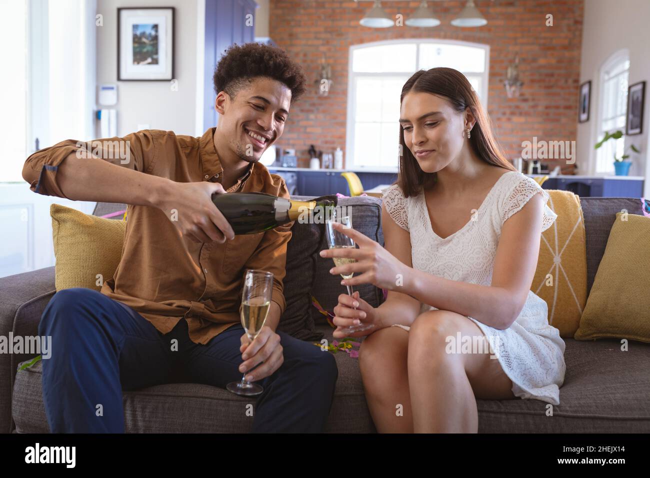 Buon giovane biraciale che versa champagne in flauto per la ragazza a casa Foto Stock