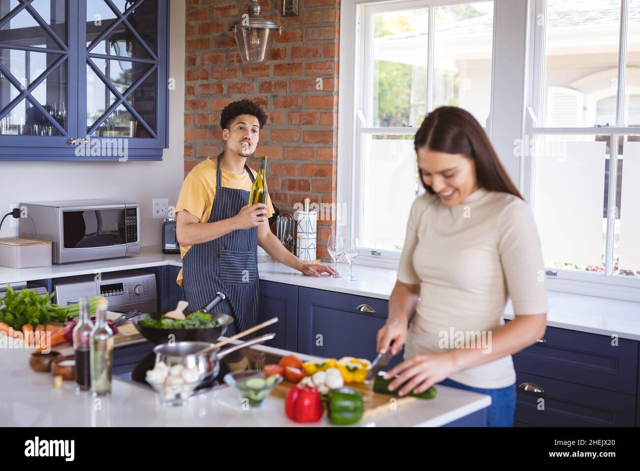 Giovane uomo che tiene la bottiglia d'olio che parla con la ragazza tritare le verdure in cucina a casa Foto Stock