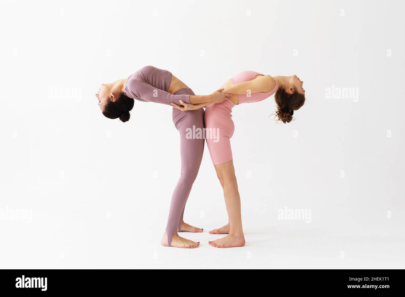 Due donne che praticano lo yoga, tengono le mani e svolgono l'esercizio Hasta Utttanasana, si piegano, si levano su uno sfondo bianco. Foto Stock