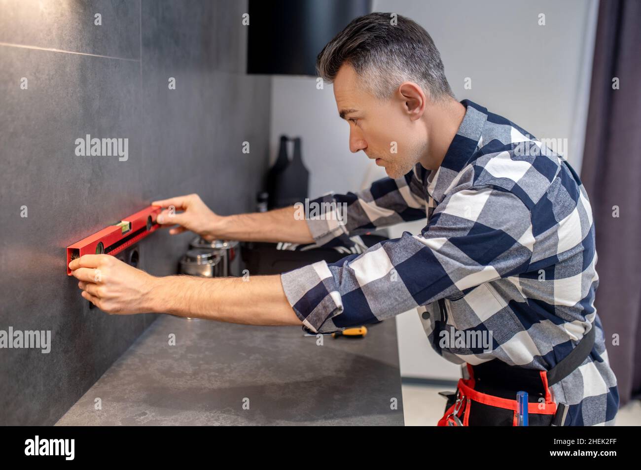 Profilo dell'uomo che tiene il misuratore di livello vicino alla parete Foto Stock