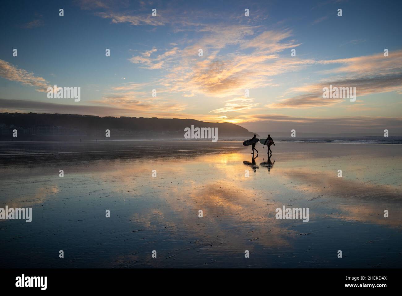I surfisti si riflettono sulle sabbie specchi mentre il sole tramonta su Westward ho! Spiaggia nel Devon del nord come tempo soleggiato è previsto per gran parte del Regno Unito per i prossimi giorni. Foto Stock